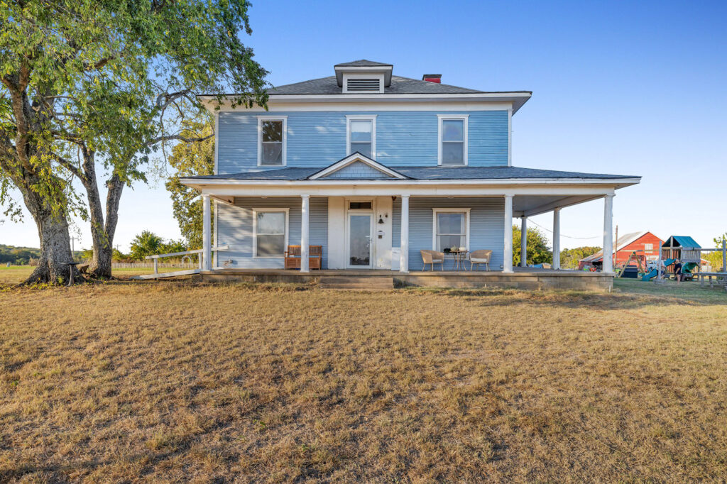 Beautiful historic farmhouse for sale in Durant, OK, featuring 52 acres of scenic rolling hills, a classic red barn, and a spacious 5-bedroom remodeled home with modern amenities and country charm.